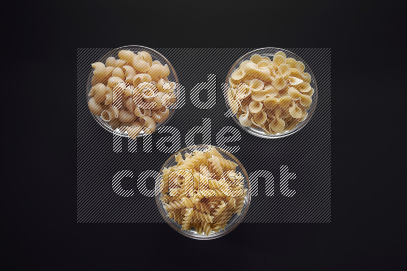 Different pasta types in glass bowls on black background