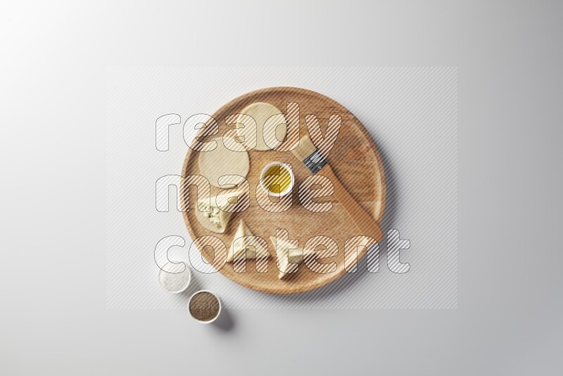 two closed sambosas and one open sambosa filled with cheese while salt, black pepper and oil with oil brush aside in a wooden dish on a white background