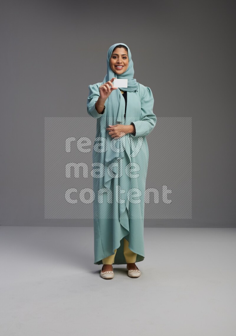 Saudi Woman wearing Abaya standing holding ATM card on Gray background