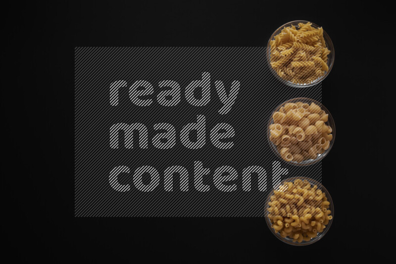 Different pasta types in 3 glass bowls on black background