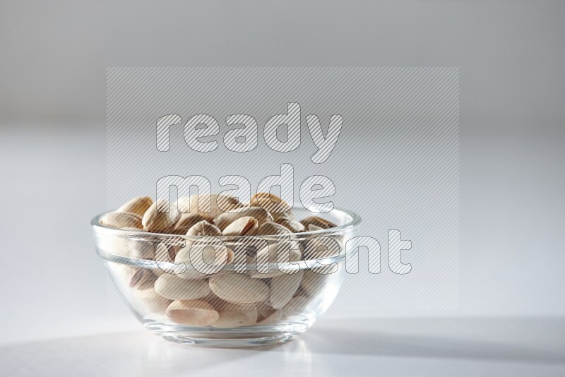 A glass bowl full of pistachios on a white background in different angles