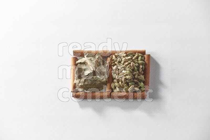 مربعان من أعواد القرفة ممتلئان بحبوب الهيل وأوراق الغار علي خلفية بيضاء