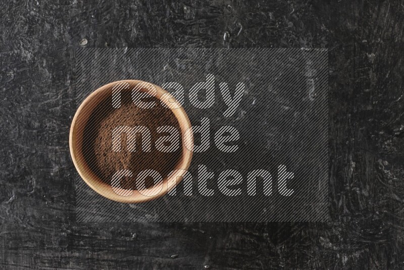 A wooden bowl full of cloves powder on a textured black flooring