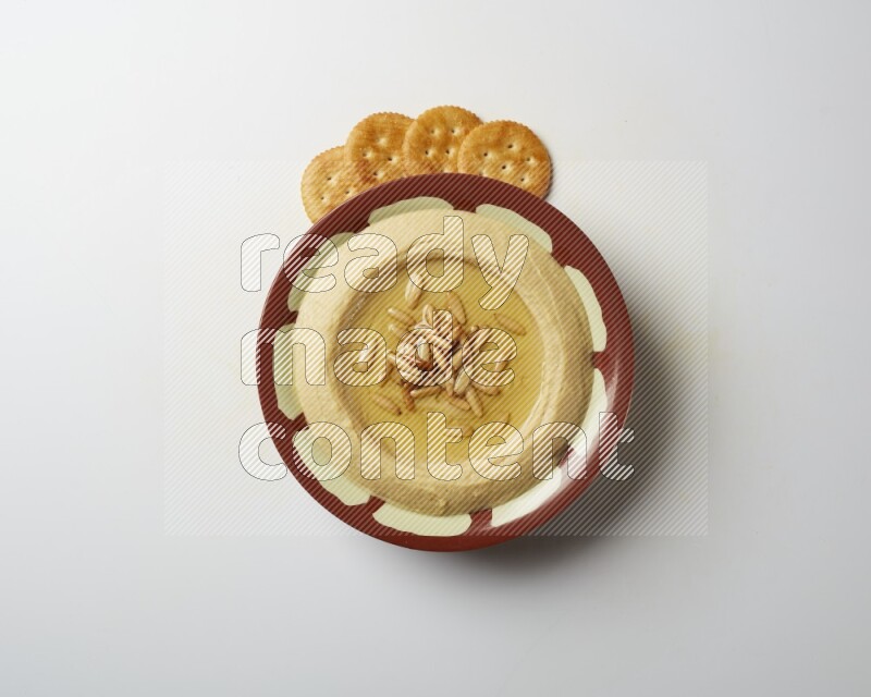 Hummus in a traditional plate garnished with pine nuts on a white background