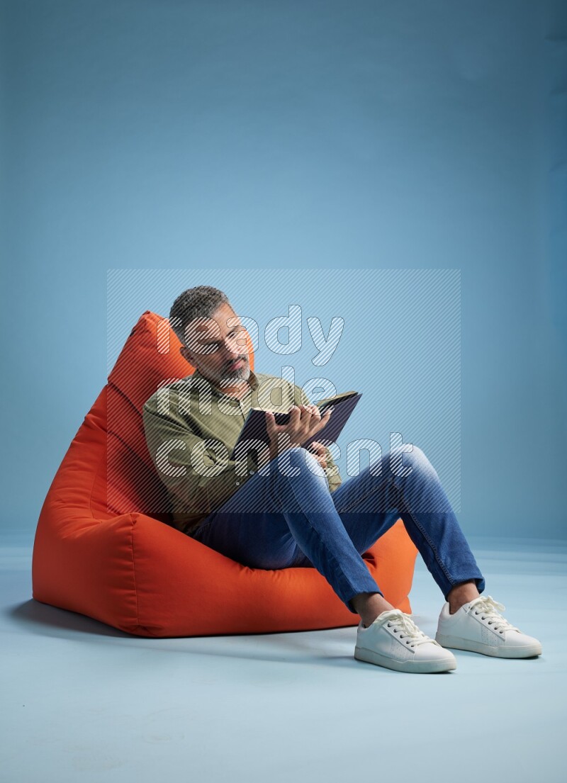 A man sitting on an orange beanbag and reading a book