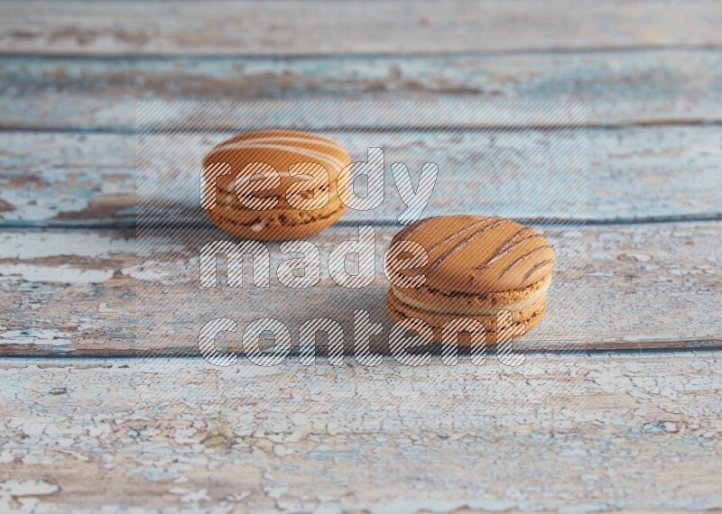 45º Shot of of two assorted Brown Irish Cream, and light brown Almond Cream macarons next to each other on light blue background