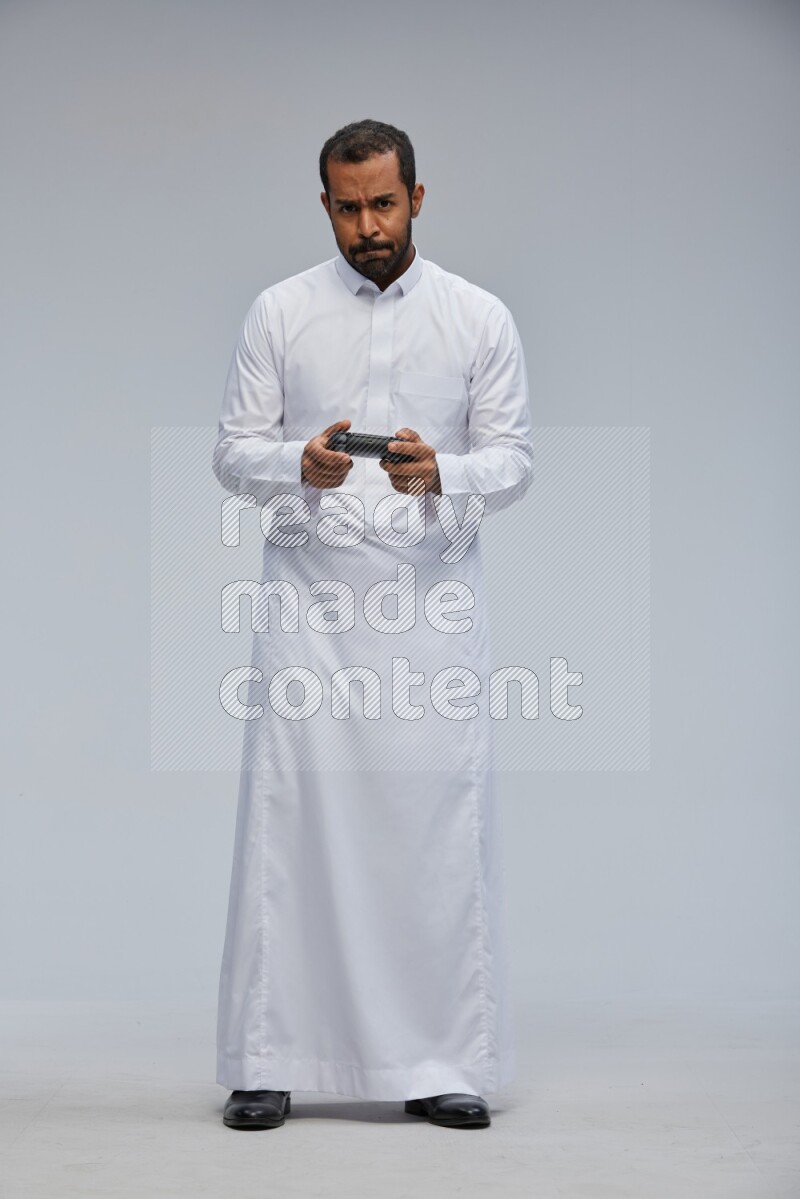 Saudi man Wearing thob standing holding joystick on Gray background