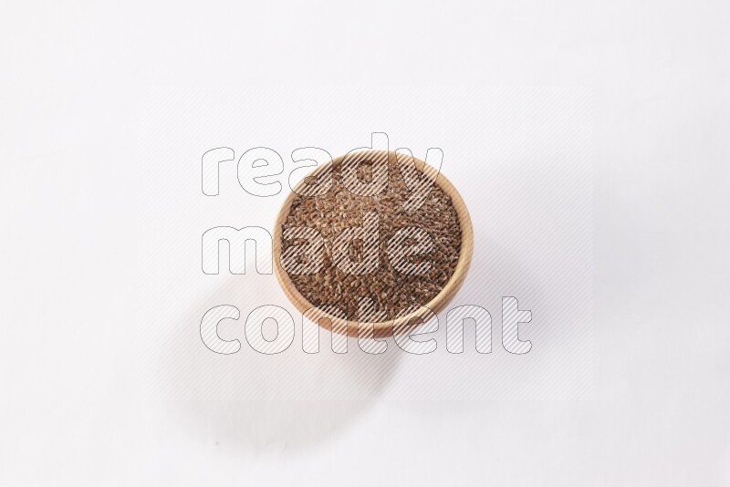 A wooden bowl full of flax seeds on a white flooring