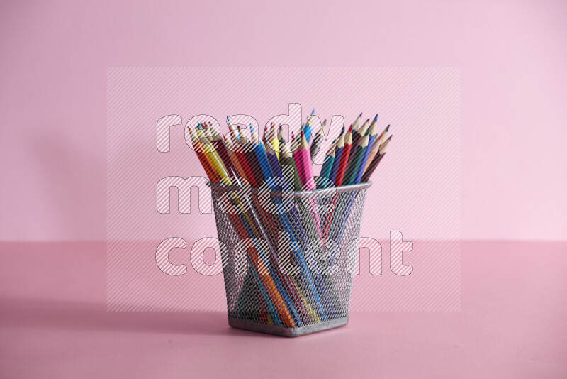 Pens, pencils and other different school supplies in a metal pen holder on rose background