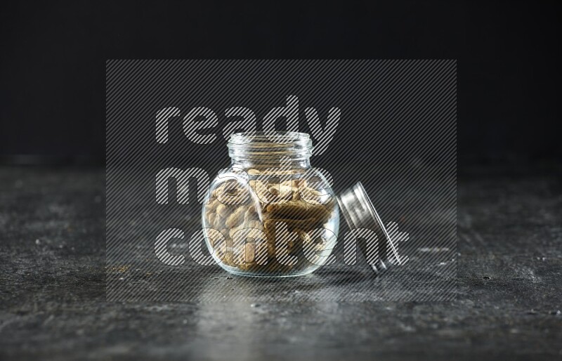 A glass spice jar full of dried turmeric whole fingers on a textured black flooring