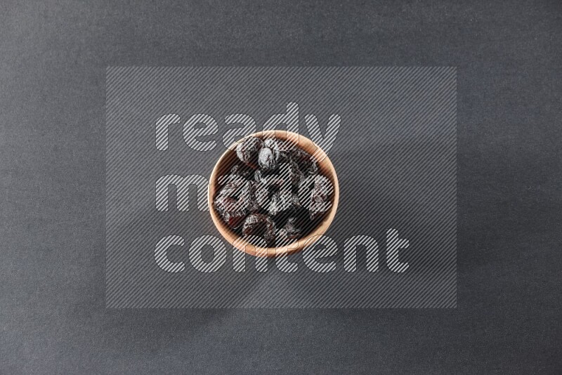 A wooden bowl full of dried plums on a black background in different angles
