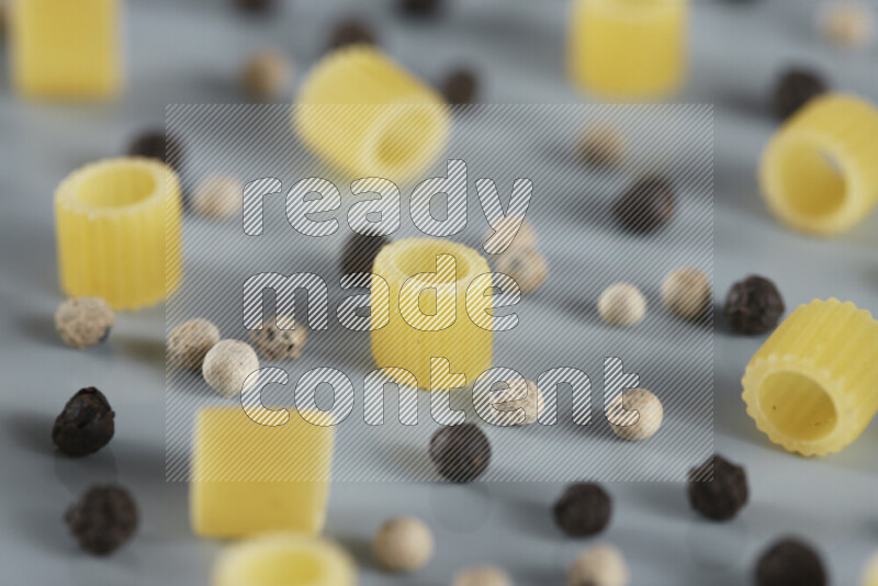 Raw pasta with different ingredients such as cherry tomatoes, garlic, onions, red chilis, black pepper, white pepper, bay laurel leaves, rosemary, cardamom and mushrooms on light blue background