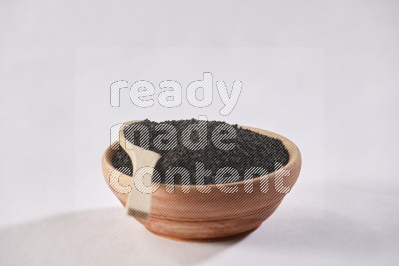 A wooden bowl and wooden spoon full of black seeds on a white flooring