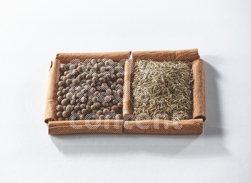 مربعان من أعواد القرفة ممتلئان ببهار الفلفل الحلو والكمون علي خلفية بيضاء