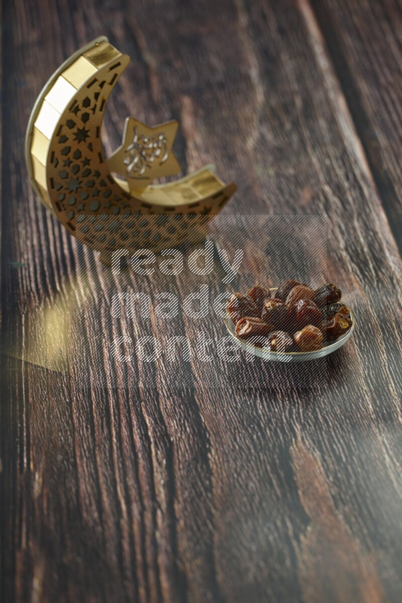 A wooden golden crescent lantern with different drinks, dates, nuts, prayer beads and quran on brown wooden background