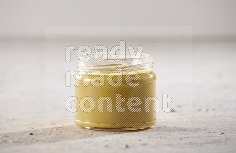 A glass jar full of mustard paste on a textured white flooring