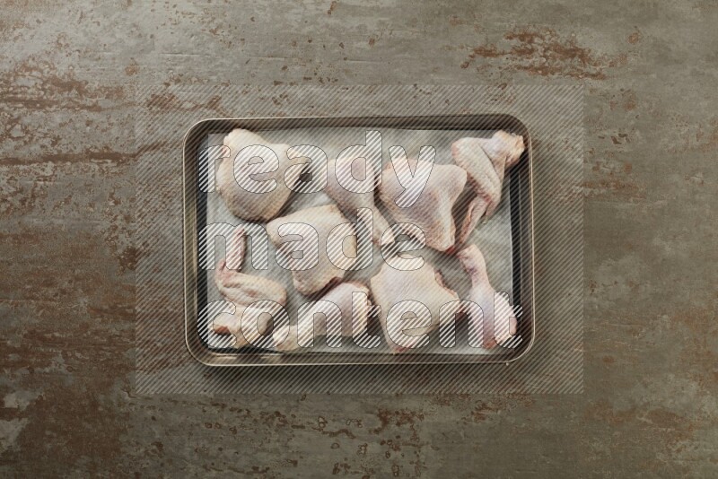 Mixed fresh chicken pieces in an oven tray on a textured rustic background