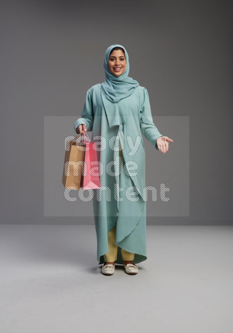 Saudi Woman wearing Abaya standing holding shopping bag on Gray background