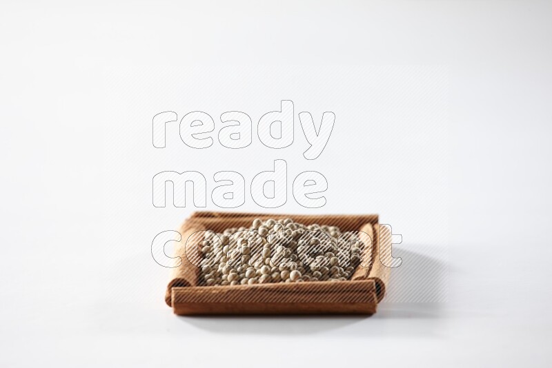 أربعة من أعواد القرفة مكونة شكل مربع بداخلها حبوب الفلفل الأبيض علي خلفية بيضاء