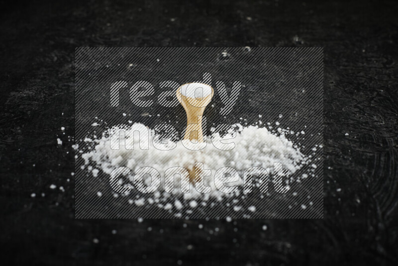 A wooden spoon full of white salt on black background