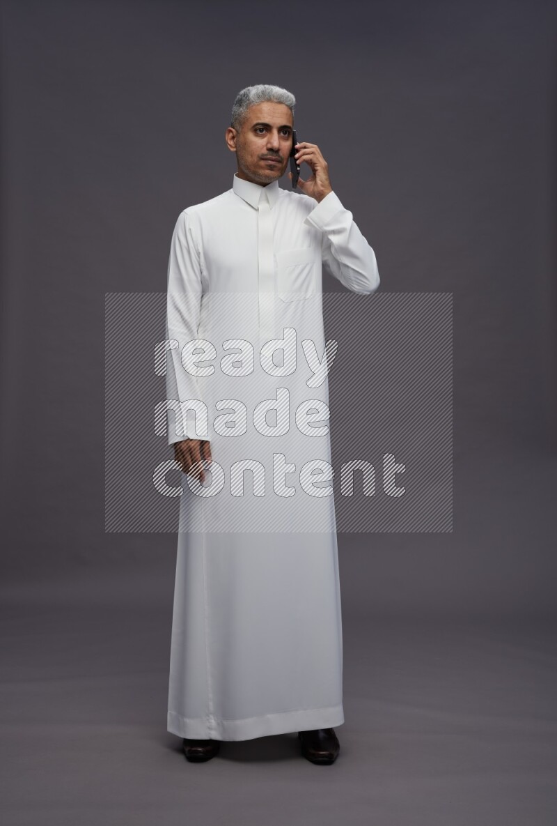 Saudi man wearing thob standing talking on phone on gray background