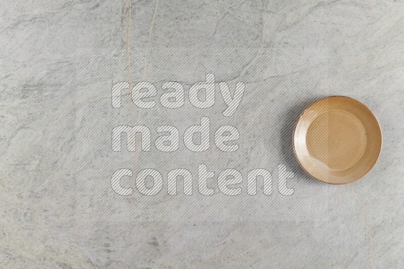 A circular beige pottery plate on grey marble background