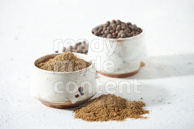 وعاءان بيج، أحدهما ممتلئ ببودرة بهار الفلفل الحلو والآخر بالحبوب مع البودرة والحبوب متناثرة على خلفية بيضاء