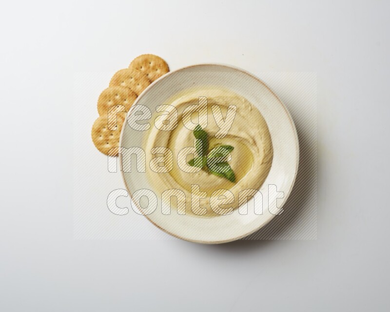 Hummus in a pottry plate garnished with mint  on a white background