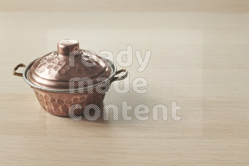 A small copper pot on light wooden background