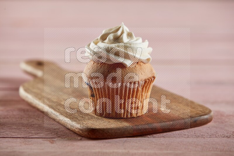 Vanilla cupcake topped with cream on a wooden board