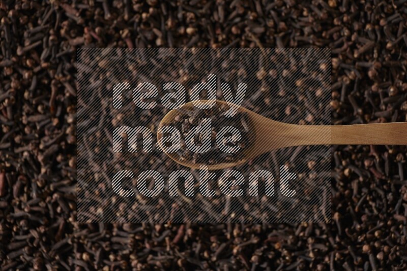 A wooden spoon full of cloves on cloves background and black flooring