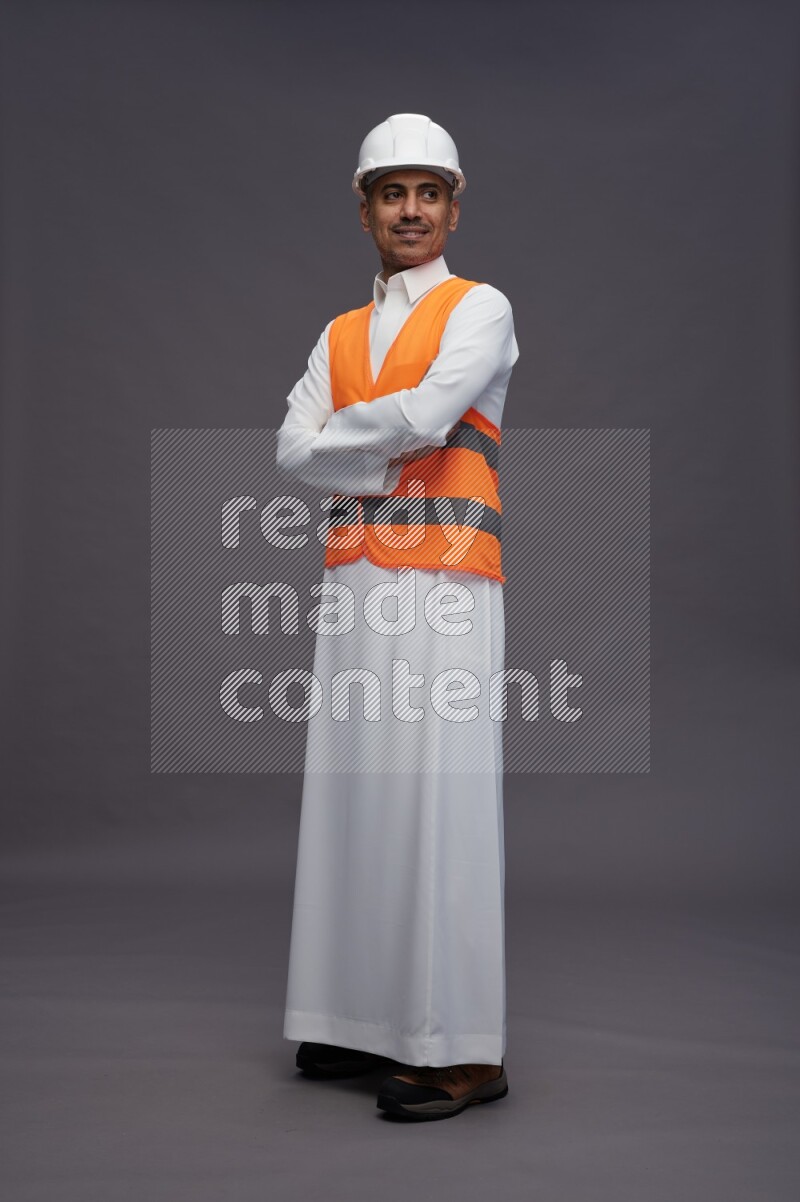 Saudi man wearing thob with engineer vest standing with crossed arms on gray background