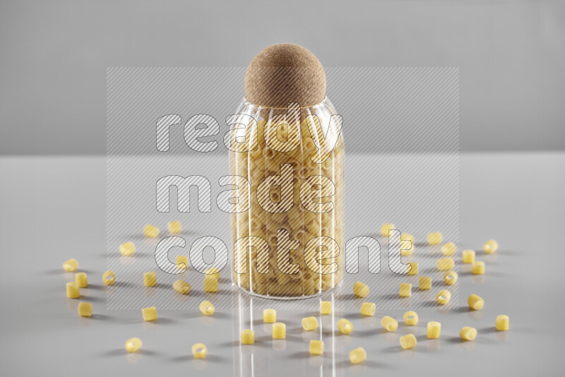 Raw pasta in a glass jar on light grey background