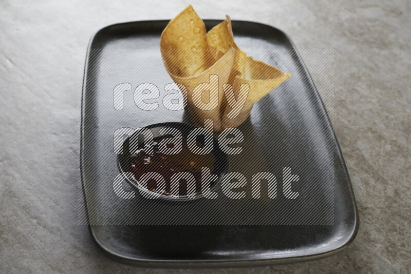 wonton cups with soy sauce ramkin on rectangle dark grey ceramic plate on grey textured counter top