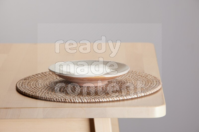 multi-colored pottery Plate placed on a big light colored straw placemat on the edge of wooden table