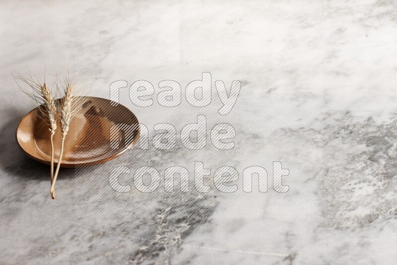 Wheat stalks on multicolored pottery plate on grey marble background