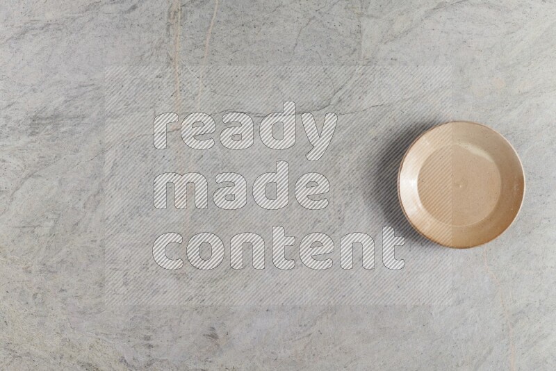 A circular beige pottery plate on grey marble background