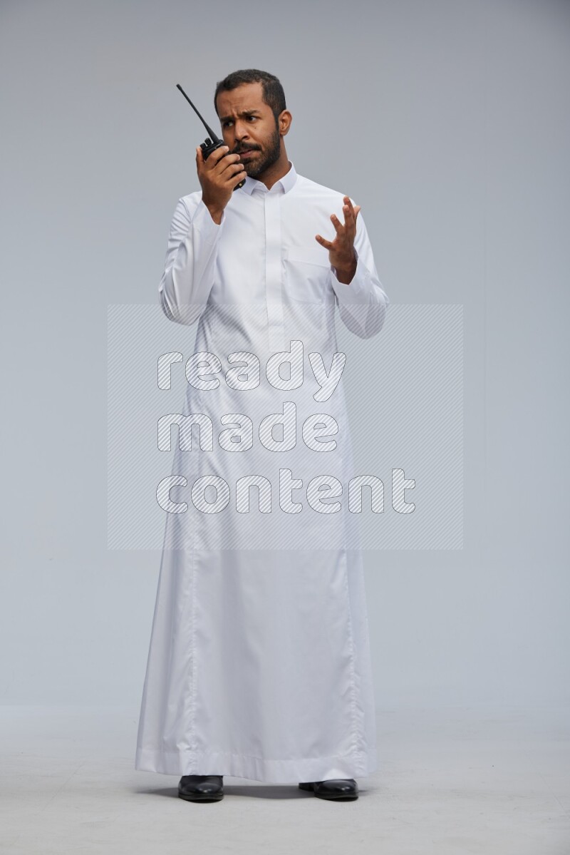 Saudi man Wearing thob standing holding walkie-talkie on Gray background