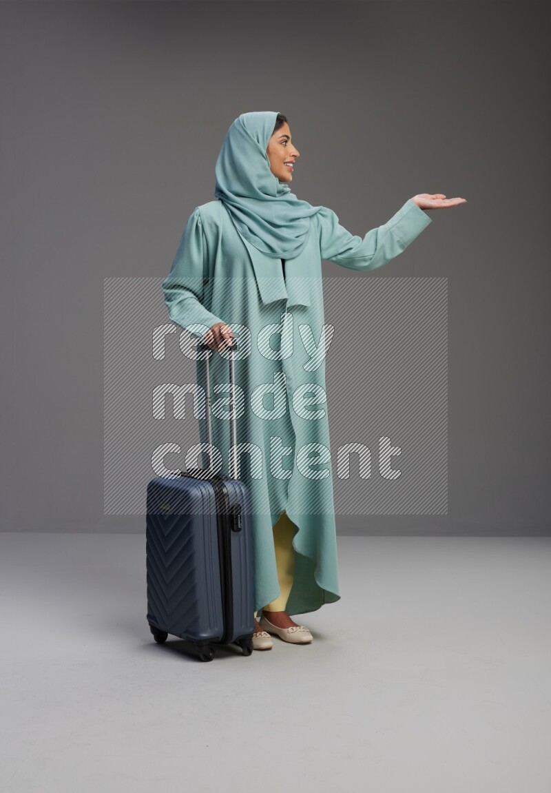 Saudi Woman wearing Abaya standing holding Travel bag on Gray background