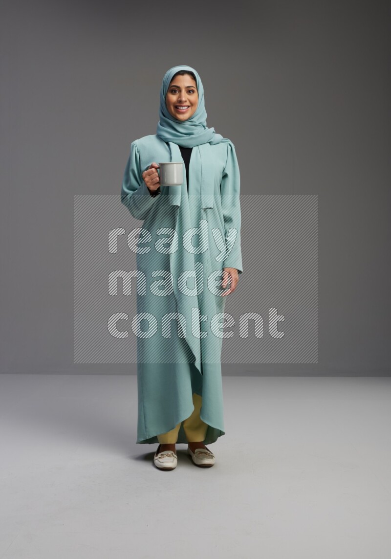 Saudi Woman wearing Abaya standing  holding a mug on Gray background