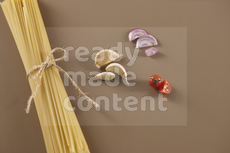 Raw pasta with different ingredients such as cherry tomatoes, garlic, onions, red chilis, black pepper, white pepper, bay laurel leaves, rosemary and cardamom on beige background