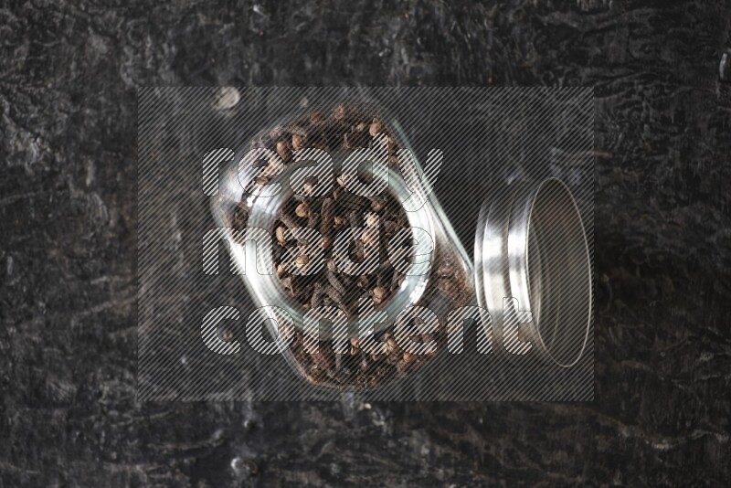 A glass spice jar full of cloves on textured black flooring