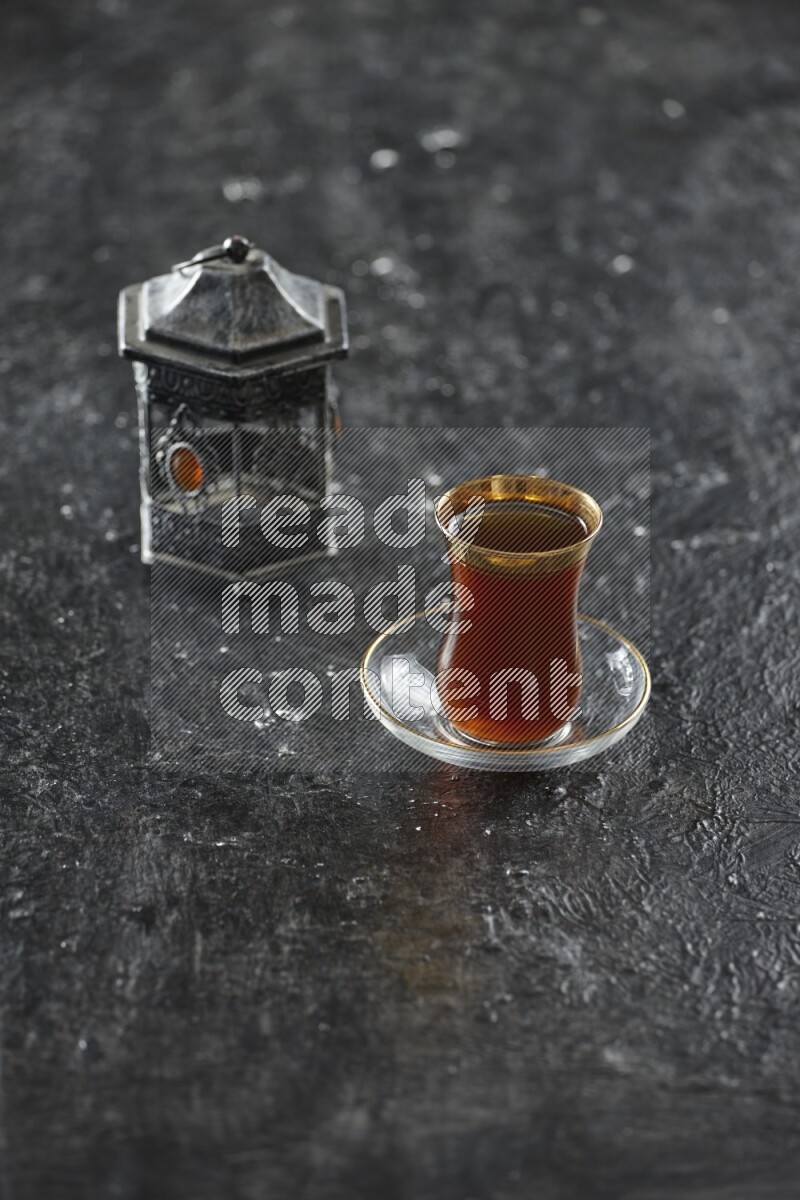 A silver lantern with different drinks, dates, nuts, prayer beads and quran on textured black background
