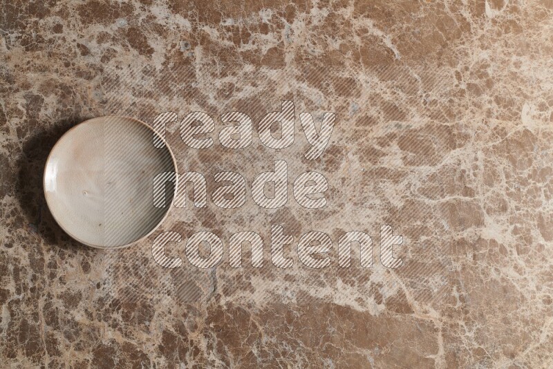 A beige pottery plate on beige marble background
