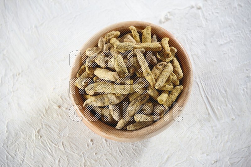 A wooden bowl full of dried turmeric whole fingers on a textured white flooring