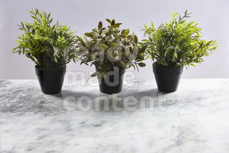 Multiple artificial plants in black pot on grey marble background