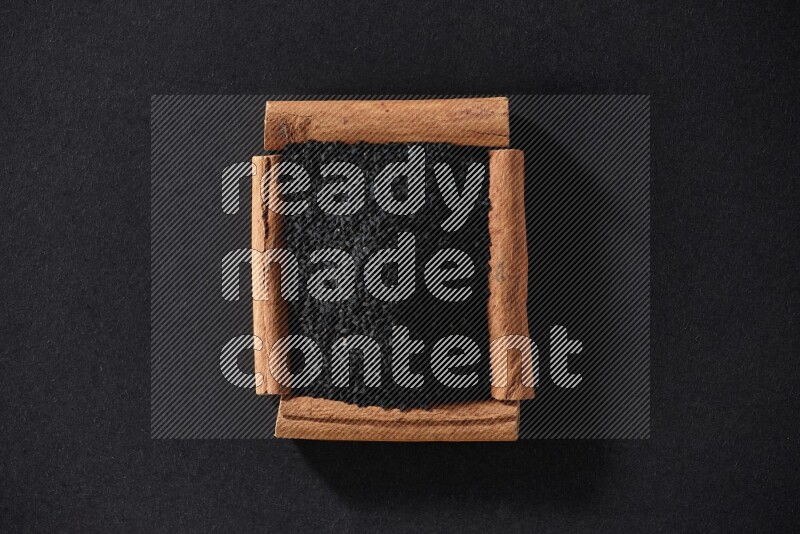 أربعة من أعواد القرفة مكونة شكل مربع بداخلها حبة البركة علي خلفية سوداء