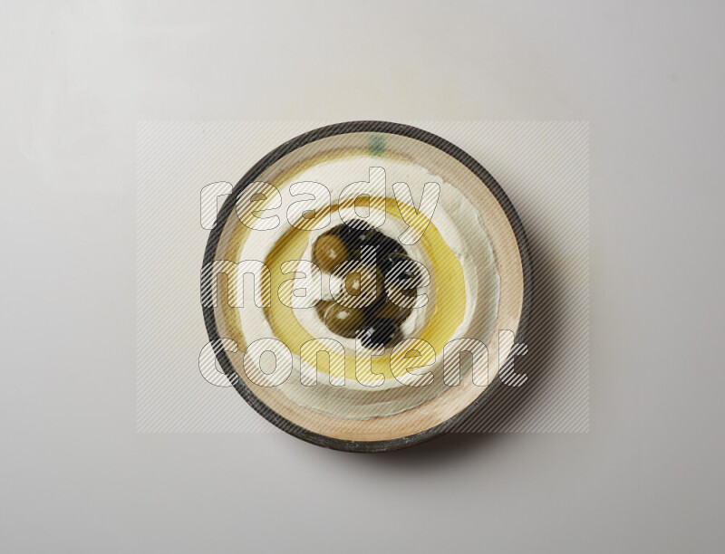 Lebnah garnished with whole black olives in a pottery plate on a white background