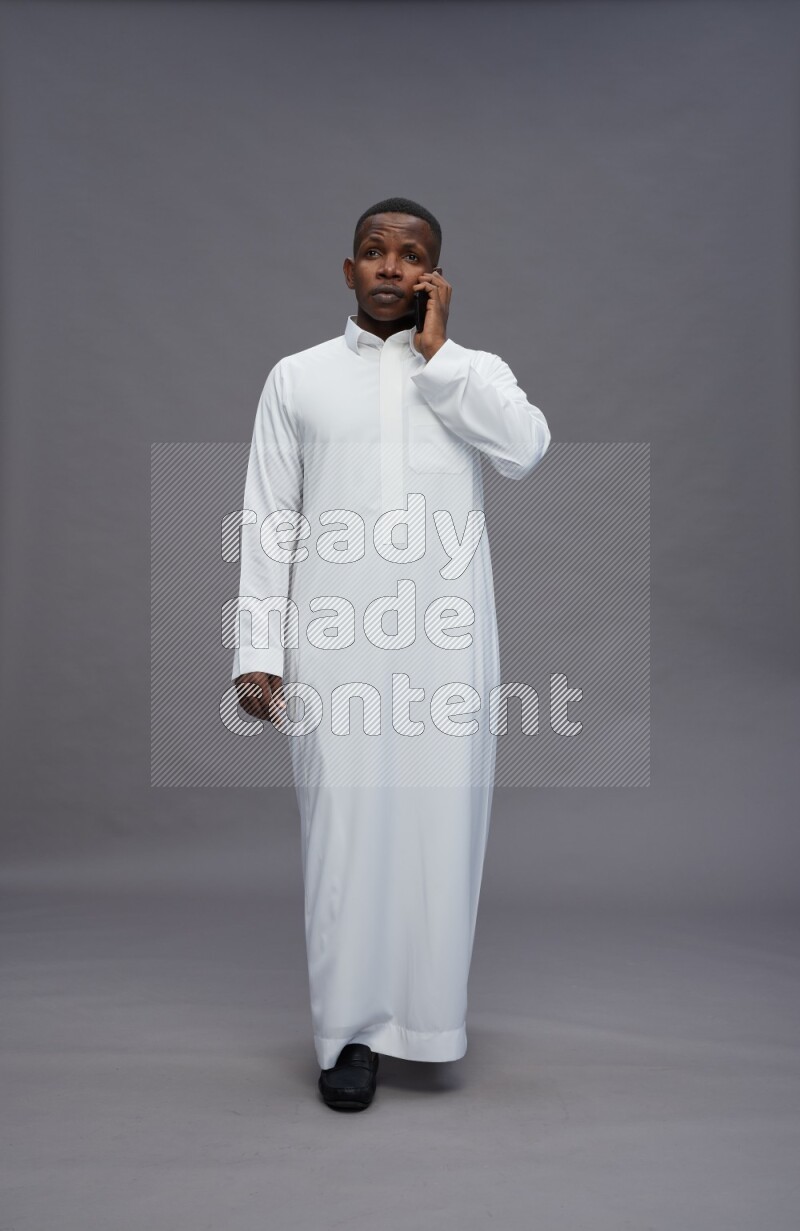 Saudi man wearing thob standing talking on phone on gray background