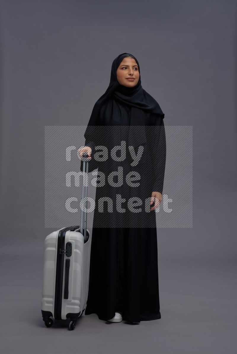 Saudi woman wearing Abaya standing holding bag on gray background